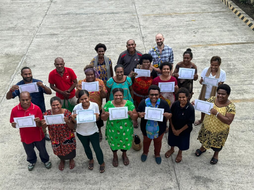 A group of people are smiling up at the camera, holding their certificate marking the completion of their training.
