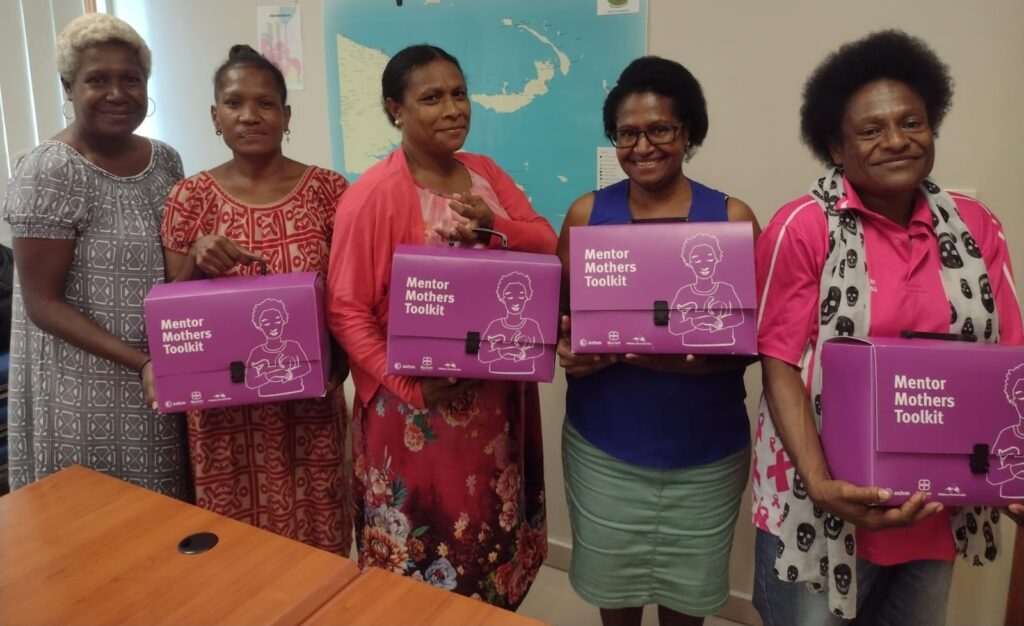 Group of women holding the Mentor Mothers Toolkits, which are a large package.